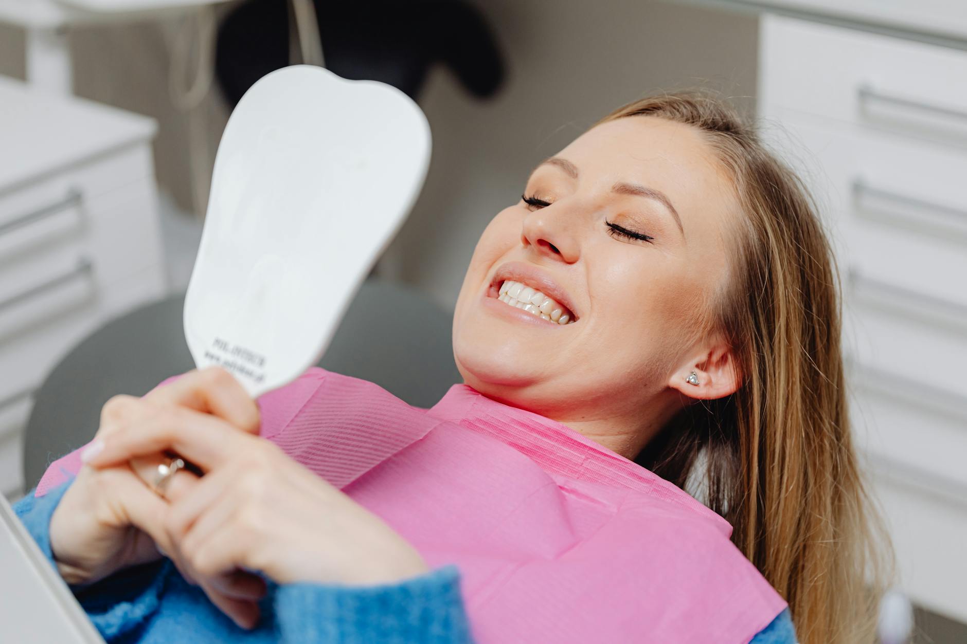 Smiling patient at a dental clinic holding a mirror after a cosmetic treatment